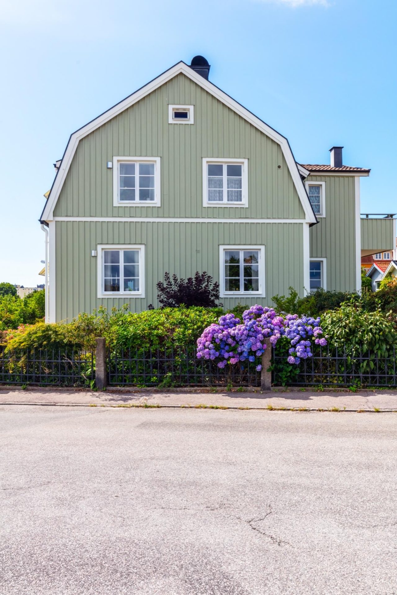 En fastighet med gröna träväggar, vita dekorativa element på fasaden, och en lummig trädgård fylld med lila hortensior