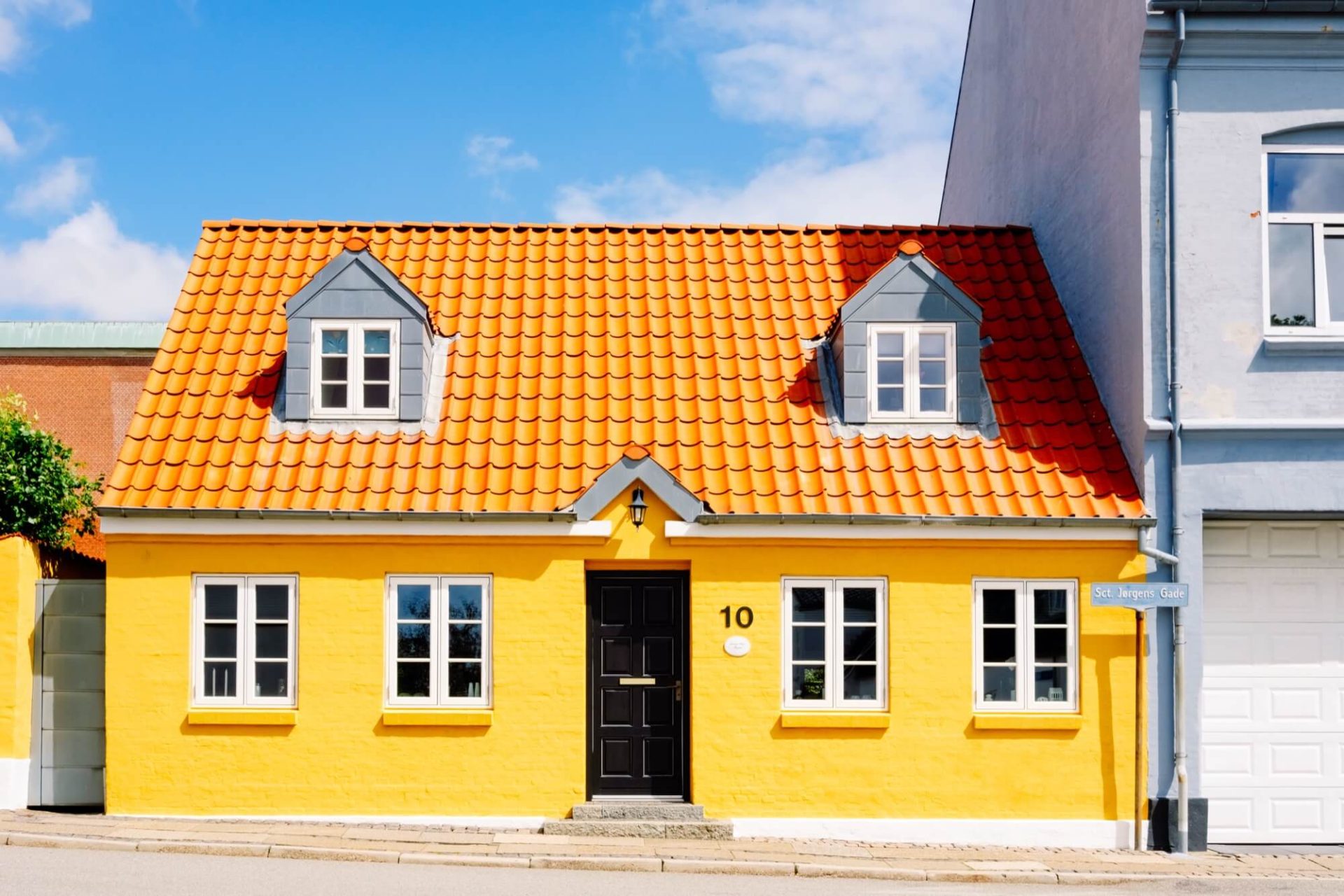 Beläget i en stads setting, detta hus fångar blickar med sin gula exteriör, orangea tak och svarta portar